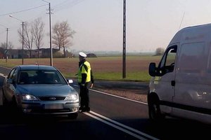 Policjant stoi na środku jezdni. Z obydwóch stron nadjeżdżają pojazdy.