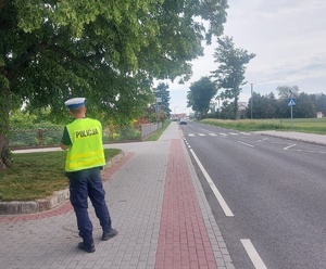 Policjant stoi na chodniku w rejonie przejścia dla pieszych. Sprawdza, z jaką prędkością porusza się nadjeżdżający samochód.