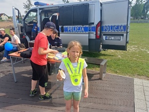 Dziewczynka ubrana w odblaskową kamizelkę na tle stoiska Policji.