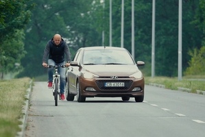 Rowerzysta jedzie drogą, a za nim samochód osobowy w bardzo bliskiej odległości.