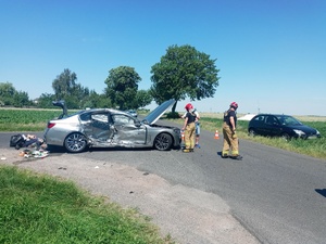 Funkcjonariusze straży pożarnej na środku skrzyżowania, gdzie stoi uszkodzone bmw