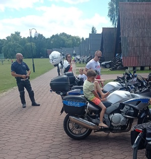 Policjant ruchu drogowego na terenie ośrodka Roma w Ostrówcach. Na jego motocyklu służbowym siedzi chłopiec.