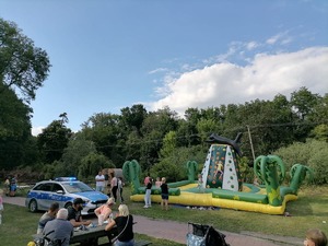 Miejsce festynu z okazji dnia dziecka. W tle dmuchańce i stoły, przy których można usiąść. Z lewej strony stoi policyjny radiowóz.