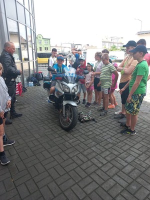 Dziedziniec KPP Żnin. Dzieci skupione wokół policyjnego motocykla. Jeden z nich siedzi na nim. Z lewej strony policjant ruchu drogowego