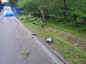 na jezdni znajduje się karetka  pogotowia z włączonymi światłami  pojazdu uprzywilejowanego, na  poboczu drogi znajduje  się kask motocyklisty