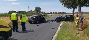 uszkodzone pojazdy znajdujące  się na pasie ruchu, dwóch policjantów oraz strażak obok, którego stoi postronna osoba