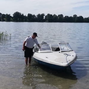 policjant  stoi koło łodzi znajdującej się na  brzegu jeziora