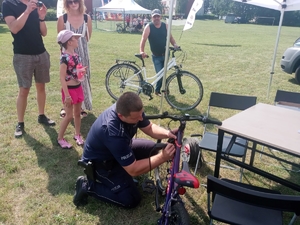 policjant  znakuje rower, w oddali inne osoby oczekują wraz rowerami