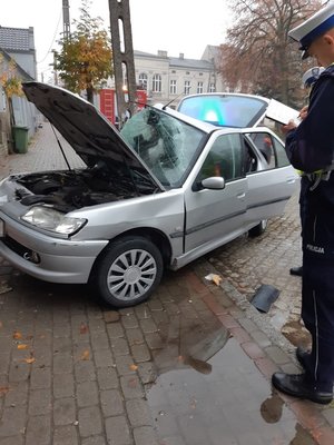 uszkodzony peugeot, który  wbił się w  słup oświetleniowy, policjant  wykonuje  oględziny pojazdu