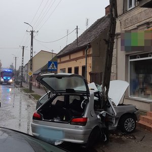 uszkodzony peugeot, który  wbił się w  słup  oświetleniowy, w  oddali stoi  wóz strażacki z włączonymi  światłami pojazdu uprzywilejowanego