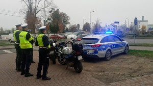 czterech policjantów stoi przy rondzie, znajdują się tam dwa  motocykle i radiowóz