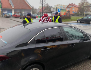 policjanci i mężczyzna  przebrany w strój Mikołaja stoją przy czarny samochodzie