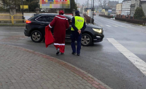 policjant i Święty Mikołaj kierują się w  stronę czarnego auta, które  stoi na skrzyżowaniu