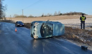 pojazd osobowy leży na  boku z widocznymi  uszkodzeniami, obok niego stoi policjant