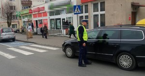 policja ruchu drogowego stoi obok czarnego samochodu, który  stoi bezpośrednio przed przejściem dla pieszych