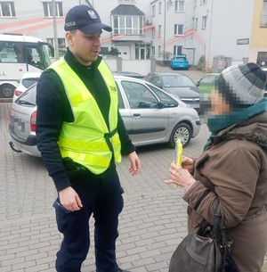 policjant  rozmawia z kobietą, która  w ręku trzyma  kamizelkę odblaskową