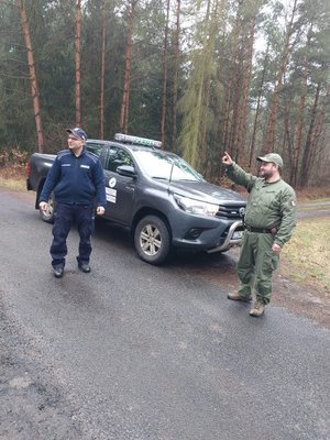 na drodze stoi strażnik leśny oraz policjant, a za nimi stoi wóz strażnika