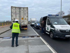 za  ciężarówką stoi funkcjonariusz inspekcji transportu drogowego, obok  niego samochód inspekcji, dostawcza i radiowóz policyjny