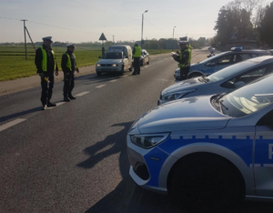 policjanci stoją na pasie  ruchu i poboczu, jeden z nich  kontroluje trzeźwość kierowcy osobówki