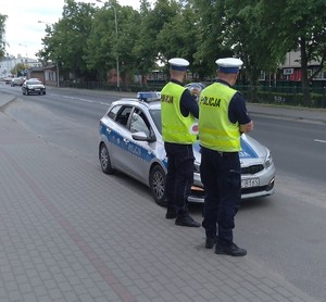 dwóch  policjantów  ruchu drogowego stoi obok radiowozu