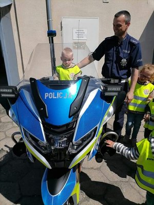 mały chłopczyk siedzi  na policyjnym motocyklu, obok niego stoi policjant