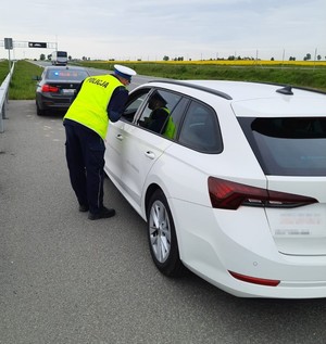 policjant  ruchu drogowego kontroluje kierowcę białej osobówki