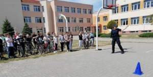 policjantka jest obok uczniów  zgormadzonych  na  boisku do koszykówki, na  którym odbywa się egzamin na kartę rowerową