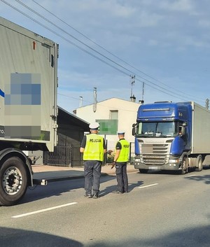 dwóch policjantów  ruchu drogowego stoi na  pasie  ruchu obok ciężarówek