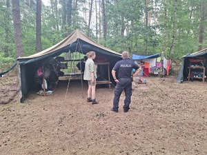 policjant i harcerka stoją wśród namiotów na terenie lasu