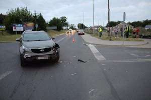 uszkodzona kia stoi na  środku skrzyżowania, w  oddali policjanci i osoby  postronne znajdują się przy leżącym motocyklu