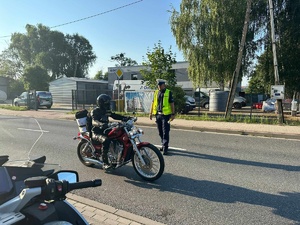 Policjant ruchu drogowego podchodzi do motocyklisty będącego na jezdni.