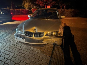 Wykostkowany plac. Panuje półmrok. Większość fotografii zajmuje uszkodzony pojazd marki BMW.