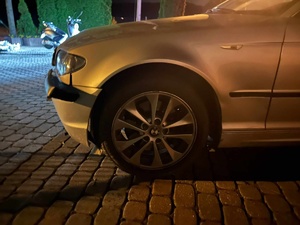 Panujący mrok. Z prawej strony fotografii stoi samochód bmw. z lewej strony za nim widać zaparkowany motorower.