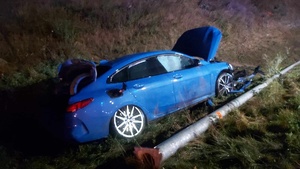 Panujący mrok. W rowie stoi uszkodzony samochód marki BMW koloru niebieskiego. Obok leży przewrócona latarnia uliczna.