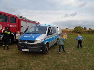 Policyjny radiowóz podczas festynu. Z lewej strony pojazd straży pożarnej. Z prawej dzieci biegające przy radiowozie.