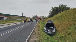 Miejsce zdarzenia. Z prawej strony w rowie stoi pojazd marki audi. Za nim na jezdni idą n/n. osoby. w oddali uszkodzony pojazd marki BMW i radiowóz policyjny i straży pożarnej.