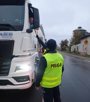 Policjant przy użyciu alkomatu sprawdza stan trzeźwości kierowcy ciągnika siodłowego.