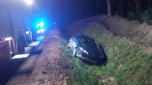 Z prawej strony pojazd marki Peugeot leżący w rowie. Z prawej strony na drodze pojazd Straży Pożarnej i Policji.