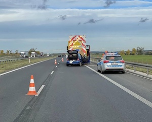 Pojazd ciężarowy i samochód osobowy, pomiędzy którymi doszło do zderzenia. Za nimi radiowóz policyjny. Miejsce zdarzenia odgrodzone pachołkami.