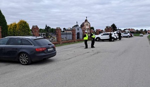 Policjanci drogówki w obrębie cmentarza obserwują ruch pojazdów i to, co dzieje się na cmentarzu.