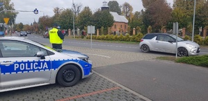 Policjant stoi przy radiowozie. Obserwuje drogę i ruch pojazdów.