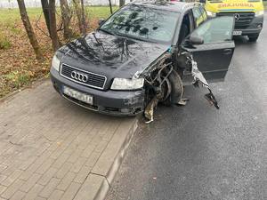 Uszkodzony pojazd marki Audi. Za nim na drodze stoi ambulans.
