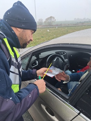 policjant  wręcza broszury oraz opaski odblaskowe kierowcy