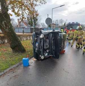 Pojazd marki VW, który leży na jezdni na boku. Wokół niego strażacy.