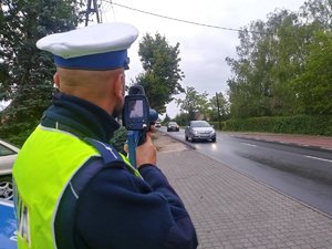 Policjant ruchu drogowego wykonuje pomiar prędkości przy użyciu laserowego miernika prędkości.