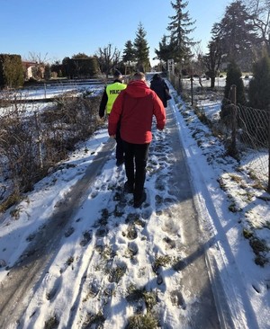 policjanci i pracownik Ośrodka  Pomocy Społecznej idą alejką ogródków  działkowych
