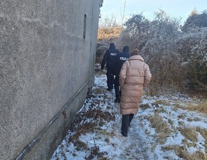 policjanci i pracownik Miejskiego Ośródka Pomocy Społecznej idą wzdłuż budynku