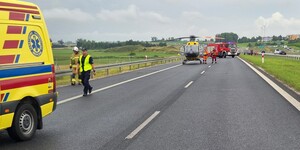 na pasie ruchu znajduje się karetka pogotowia obok przechodzi policjant, na dalszym planie znajduje się śmigłowiec Lotniczego Pogotowia Ratunkowego