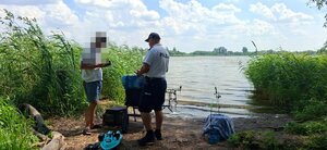 policjant  stoi obok wędkarza nad brzegiem jeziora