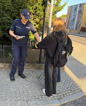 policjantka wręcza element odblaskowy dwóm dziewczynom ubranych w ciemne rzeczy